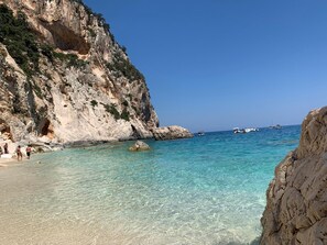 A coastal scene with clear turquoise waters, rocky cliffs, and boats. - Case Vacanza "Le Cale - Cala Goloritzè" (Tortolì)