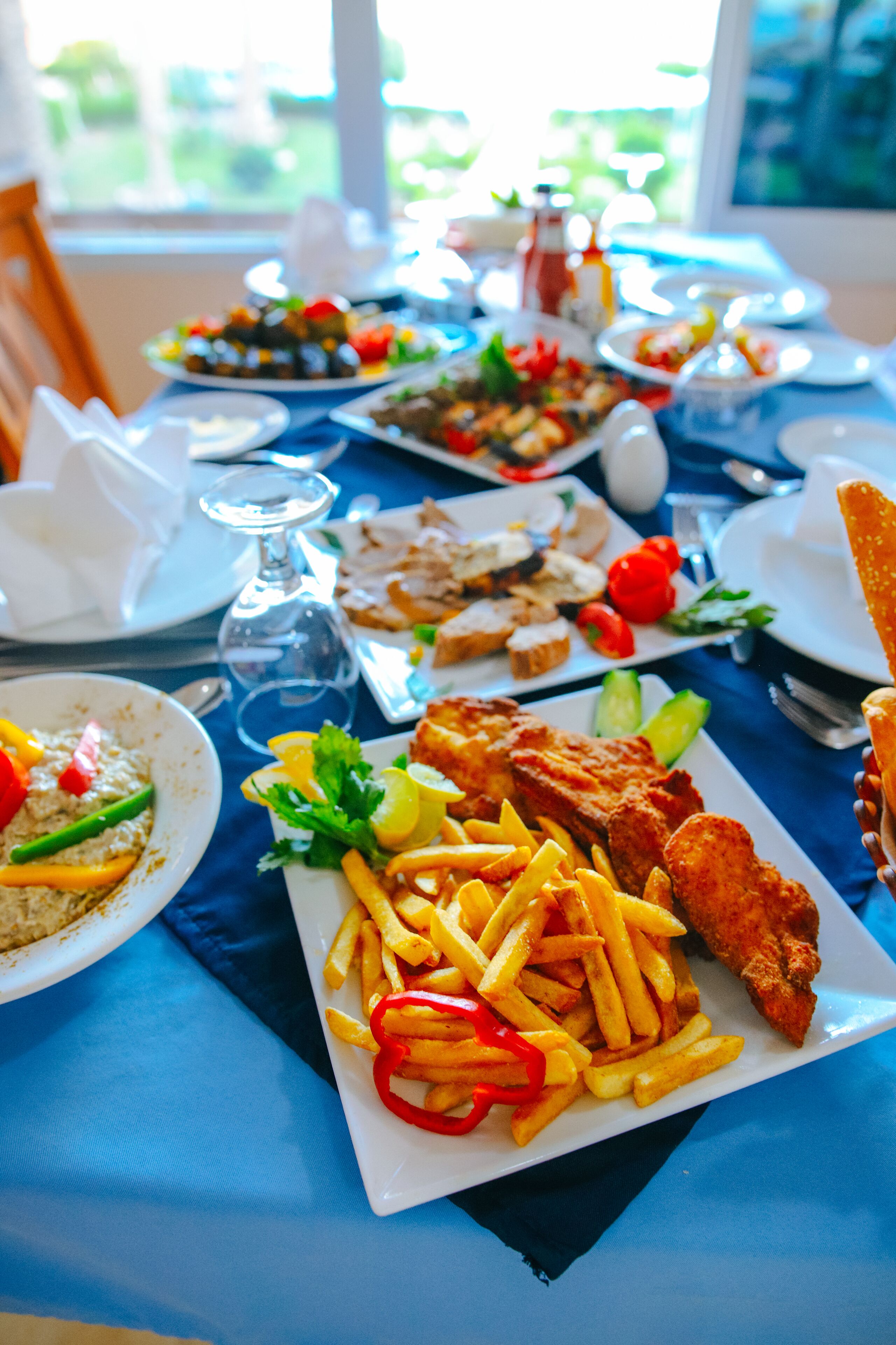 Une table à manger avec différents plats, notamment du poisson frit, des frites et des salades.