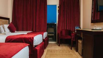 A hotel room with two beds, a desk, a chair, and a view through a window.