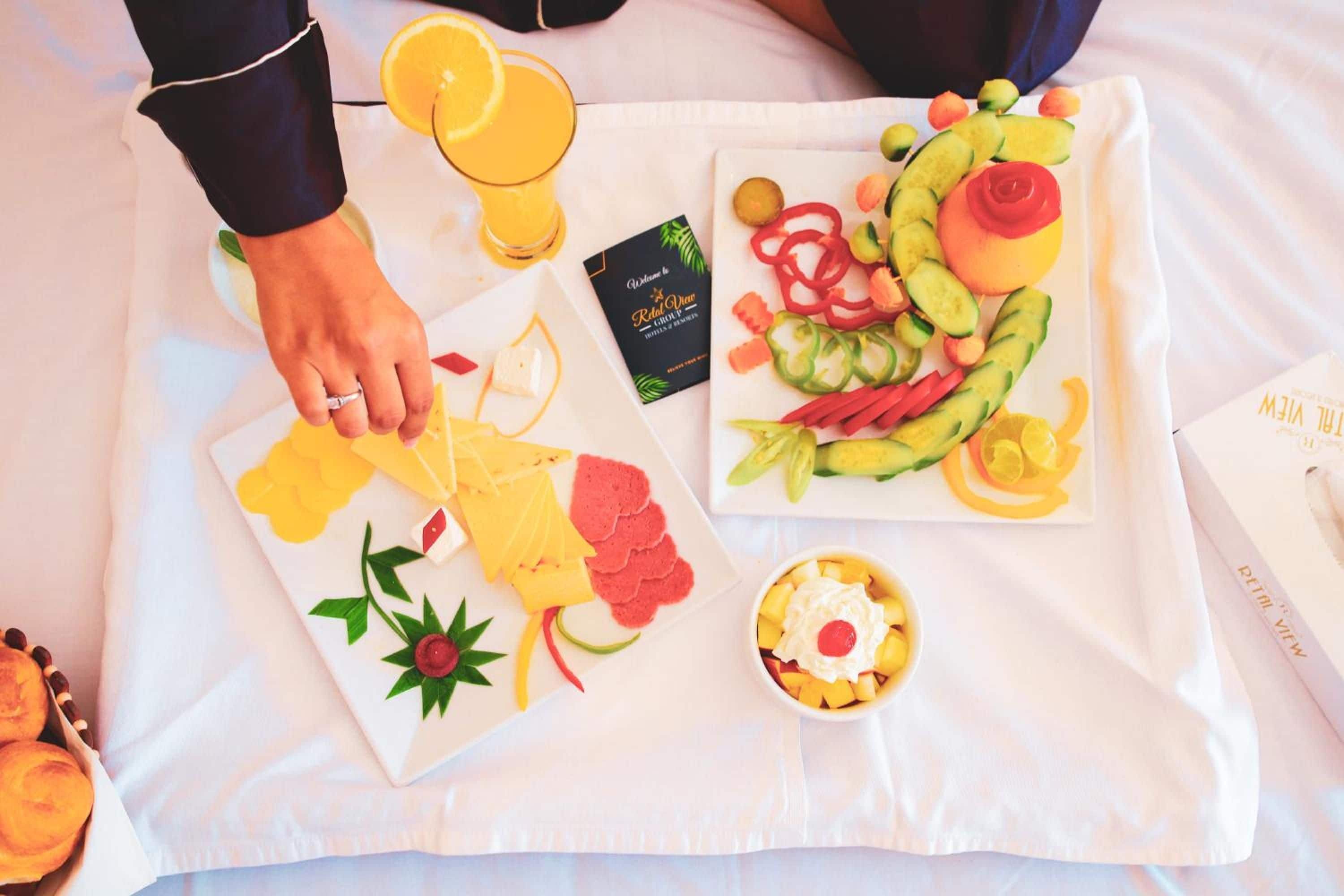 Een ontbijfwagen met diverse soorten fruit, een glas sinaasappelsap, een kleine kom yoghurt met een kersje, en een boek getiteld 'Ritual View'.