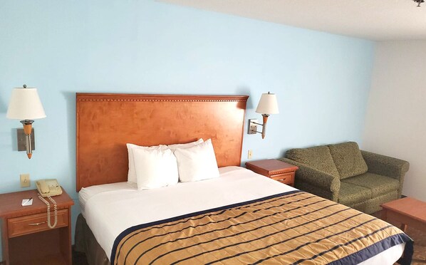 Una habitación de hotel con una cama grande, dos mesitas de noche, un sillón verde y un cabecero de madera.