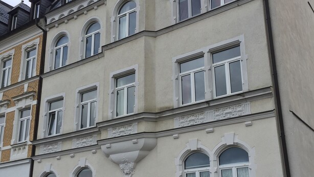 Ein mehrstöckiges Gebäude mit klassischer Architektur, darunter Bogenfenster und dekorative Stuckleisten.