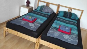 Ein Doppelbett mit Holzgestell, zwei Kissen und ein Nachttisch mit einer Lampe.