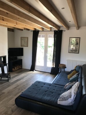 A living room with a sofa, a television, a fireplace, and a window with curtains. - Maison Mango à Capbreton Bien Placée au Bouheben en Bordure de Foret (Capbreton)