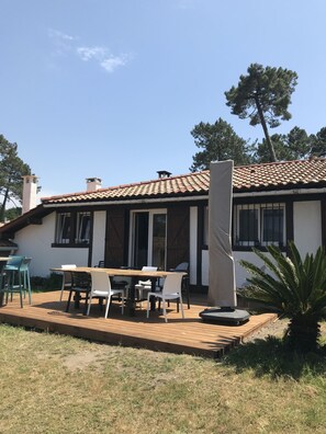 A house with a tiled roof, a patio with a table and chairs, and a large tree in the background. - Maison Mango à Capbreton Bien Placée au Bouheben en Bordure de Foret (Capbreton)