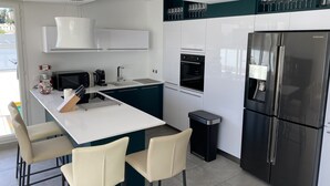 Una cocina moderna con una isla central, taburetes de bar, un refrigerador y un microondas.