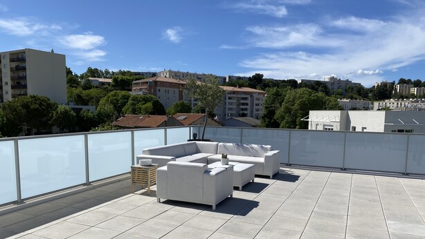Terraza en la azotea con un sofá blanco, una mesita y una planta en maceta.