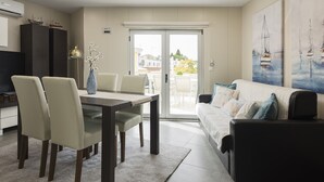 A modern living room with a dining area, a sofa, and a painting of sailboats. - Marina Luxor - Vilamoura (Vilamoura)