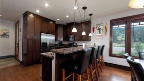 A modern kitchen with wooden cabinets, stainless steel appliances, a granite countertop, and pendant lighting.