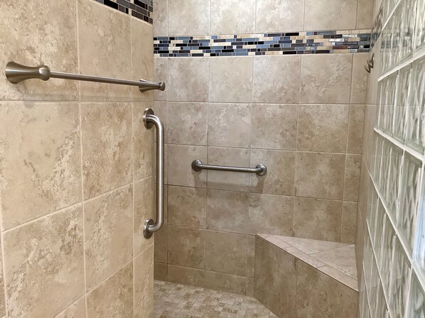 Ducha con azulejos color beige, un pasamanos y suelo de baño revestido de azulejos.
