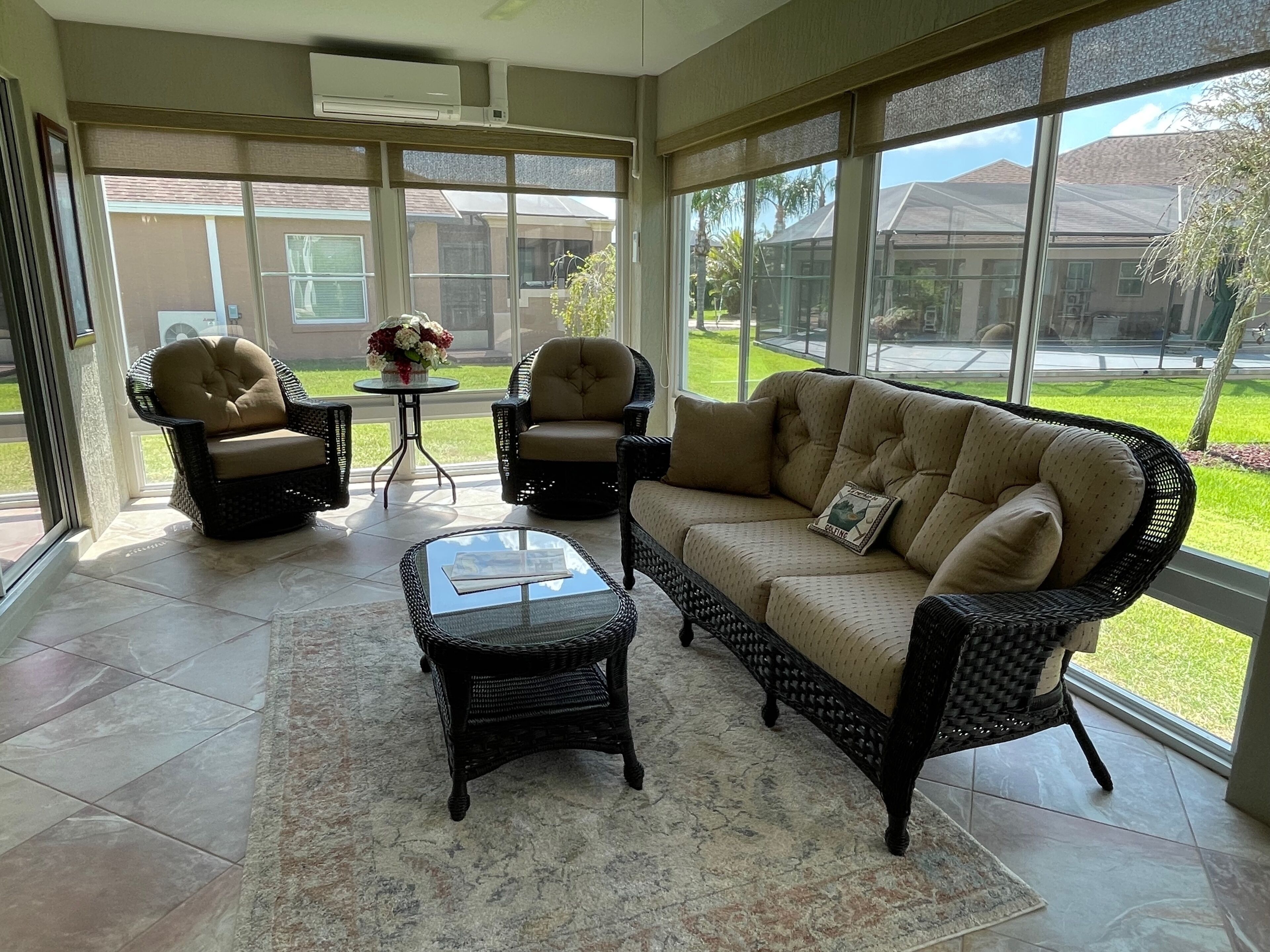 A sunlit room with a sofa, two armchairs, a coffee table, and a small table with a vase of flowers.