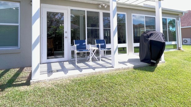 Ein überdachter Patio-Bereich mit Grill, zwei Stühlen und einer Glasdoor, die zu einem Haus führt.