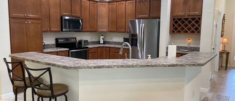 A kitchen with wooden cabinets, granite countertops, a stainless steel refrigerator, and a built-in microwave.