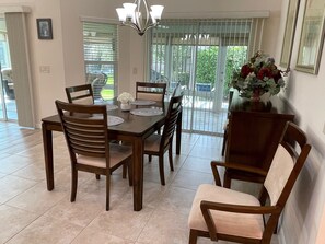 Comedor con mesa dispuesta para cuatro personas, sillas, una araña y vista a través de un ventanal.