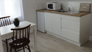 Eine kleine Küche mit weißen Schränken, einer Mikrowelle und einem Spülbecken. Es gibt einen Tisch mit einem Stuhl und einem Topf mit Pflanze.