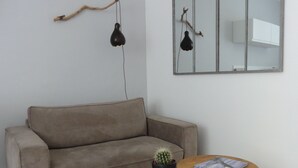 Ein Wohnzimmer mit einem beigen Sofa, einem runden Couchtisch mit einem Topf-Kaktus und einem Wandspiegel.
