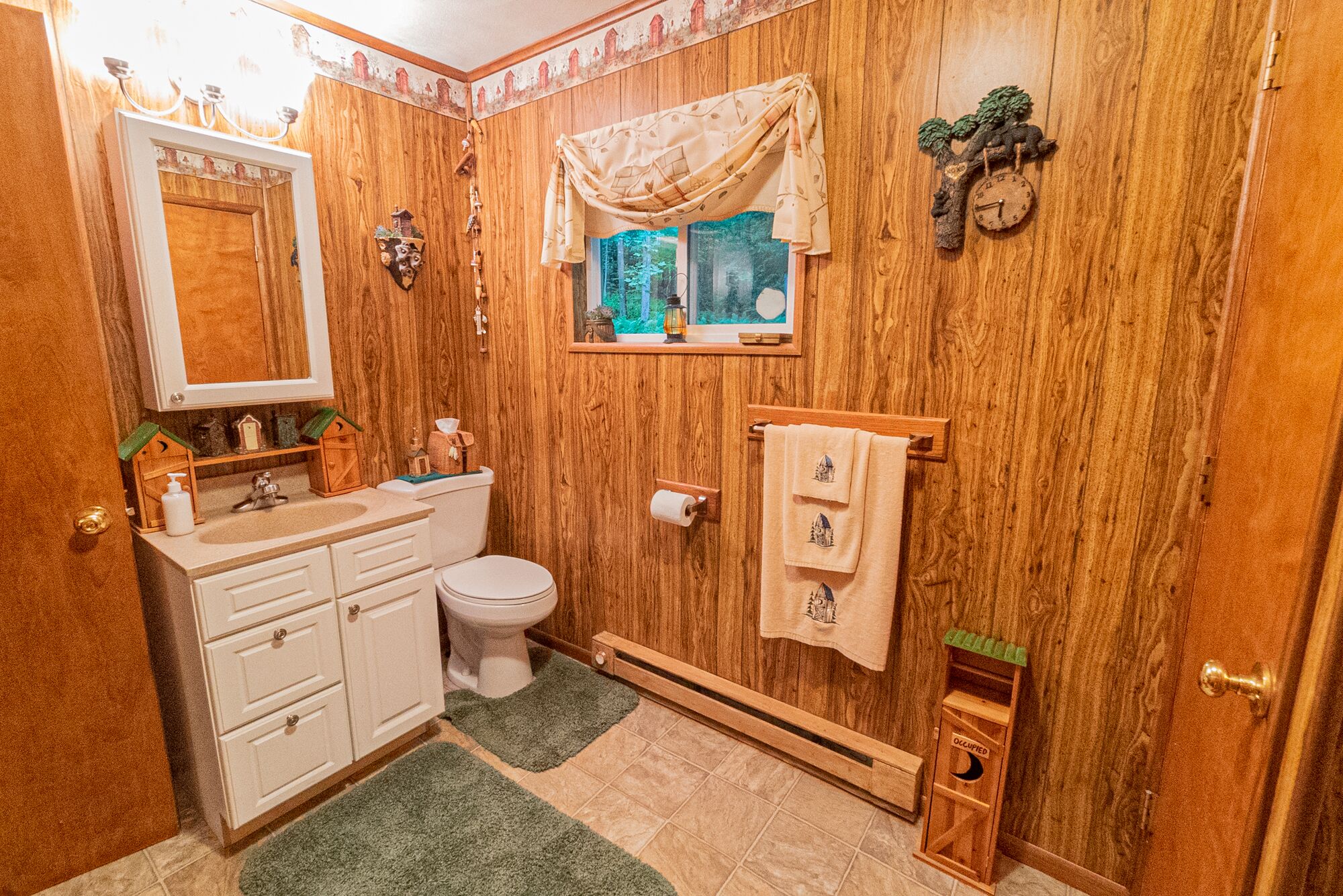 A wooden-paneled bathroom with a toilet, sink, and towel rack.