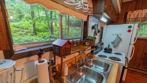 Uma cozinha rústica com bancada de madeira, pia, fogão e janela com vista para uma floresta.