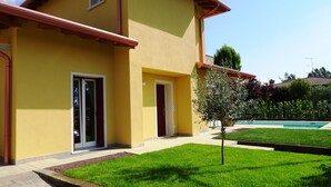 A yellow building with two doors, a small tree, and a swimming pool in the background. - Villa Massimiliano, with private heated pool and garden (Solarolo)