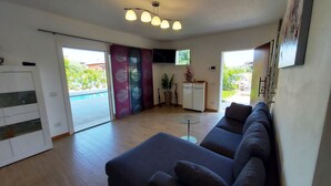 A modern living room with a sofa, a small table, and a kitchen area with a fridge and a TV. - Villa Massimiliano, with private heated pool and garden (Solarolo)