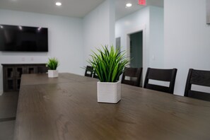 A conference room with a long wooden table, white chairs, and a potted plant in the center.