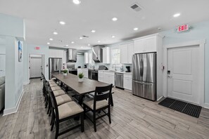 A modern kitchen with white cabinets, stainless steel appliances, and a long dining table with chairs.