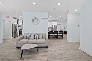 A modern kitchen with stainless steel appliances, a dining area with a table and chairs, and a living area with a sofa and a clock on the wall.