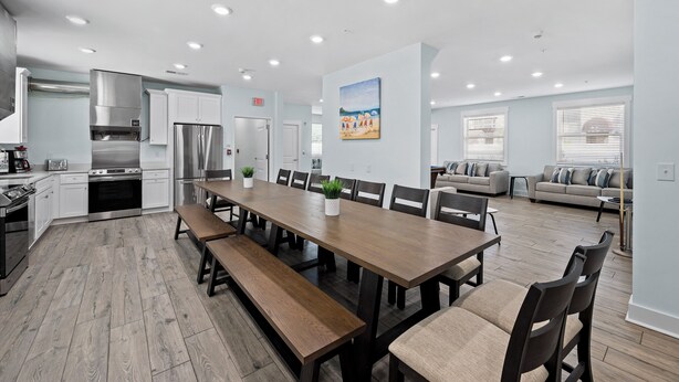 A modern kitchen with a long dining table, built-in appliances, and a seating area with a sofa and chairs. - MAIN EVENT HOME 20beds/19baths CINEMA+AMENITIES+Pool ONLY 350ft to beach!!! (Myrtle Beach)