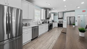 A modern kitchen with stainless steel appliances, white cabinetry, and a wooden floor. - MAIN EVENT HOME 20beds/19baths CINEMA+AMENITIES+Pool ONLY 350ft to beach!!! (Myrtle Beach)
