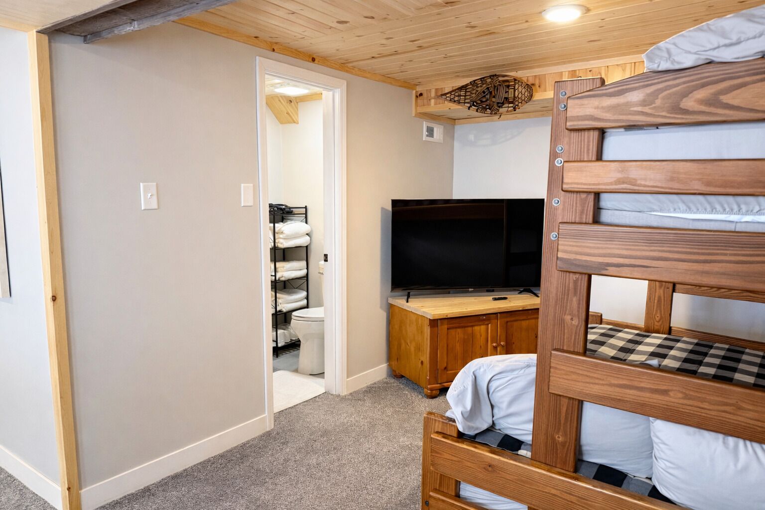 A room with a bunk bed, a television on a wooden cabinet, and a bathroom visible through an open door.