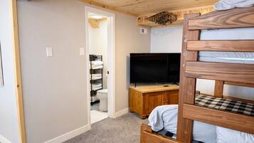 A room with a bunk bed, a television on a wooden cabinet, and a bathroom visible through an open door.