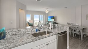 A modern kitchen with a granite countertop, stainless steel sink, and white cabinetry. - Gulf Front, NW Top Floor Condo on Side Street in MXB ~ Surfside 17 (Mexico Beach)
