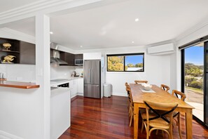 Una cocina moderna con armarios blancos, electrodomésticos de acero inoxidable y un comedor con mesa y sillas de madera.