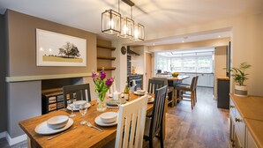 A dining area with a wooden table set for four, chairs, a vase with flowers, and a hanging light fixture.