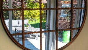 A view through a window with a grid pattern, revealing a patio area with a table, chairs, and a green trash can.