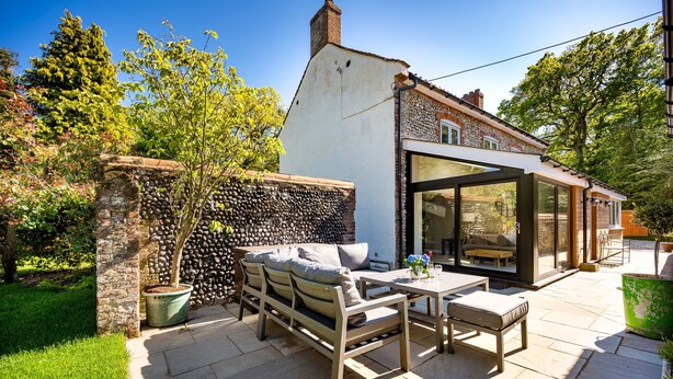 A patio with a wooden table and chairs, a stone wall, and a potted tree.
