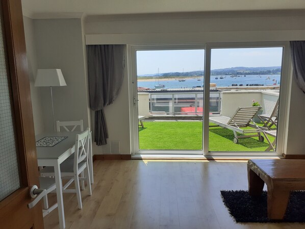A room with a view of a green lawn and a body of water.