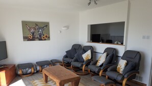 A modern living room with a wooden coffee table, grey recliner chairs, a painting on the wall, and a television on a wooden stand. - As close to the beach as you can possibly get !!!  uninterrupted estuary views (Exmouth)