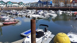 A marina with various boats docked, a wooden pier, and colorful buildings in the background. - As close to the beach as you can possibly get !!!  uninterrupted estuary views (Exmouth)
