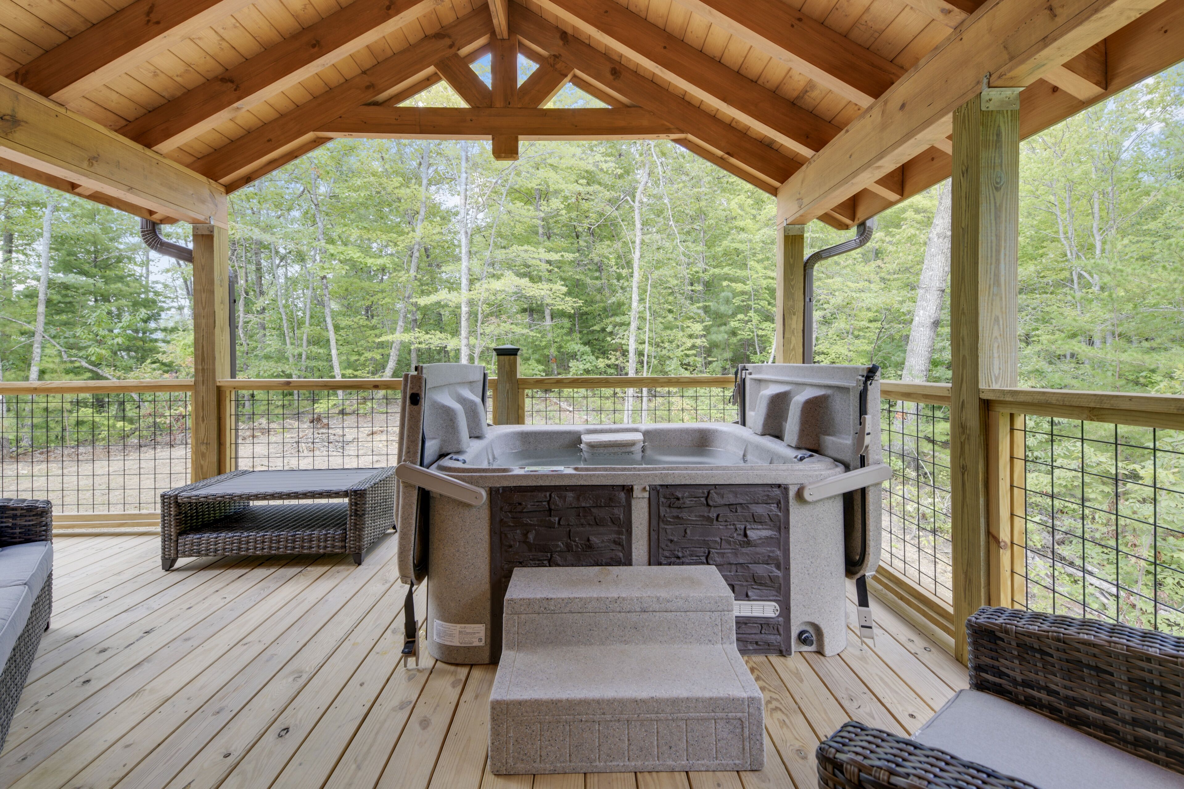 A covered outdoor deck with a hot tub, wicker furniture, and a stone bench.