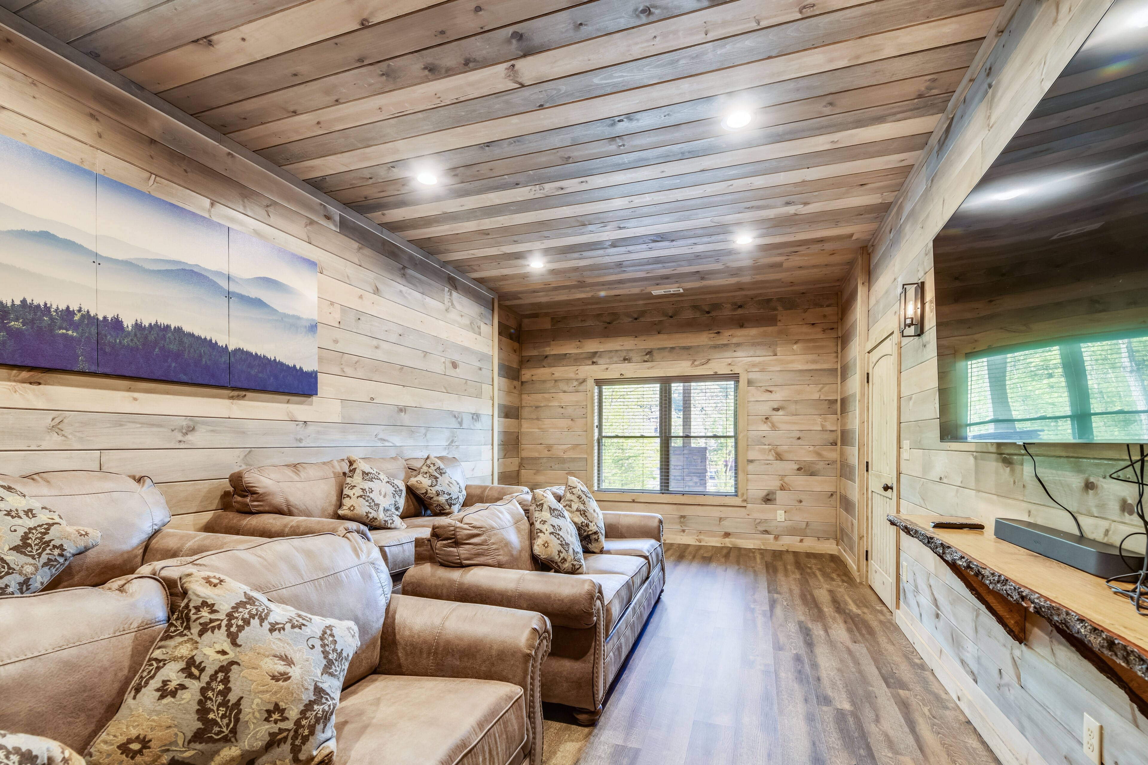 A cozy cabin interior with wooden walls, a large window, and a flat-screen TV on a wooden counter.