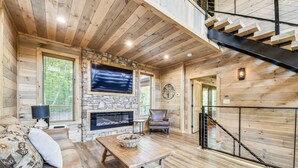 A cozy log cabin interior with a stone fireplace, a comfortable sofa, a wooden coffee table, and a staircase.