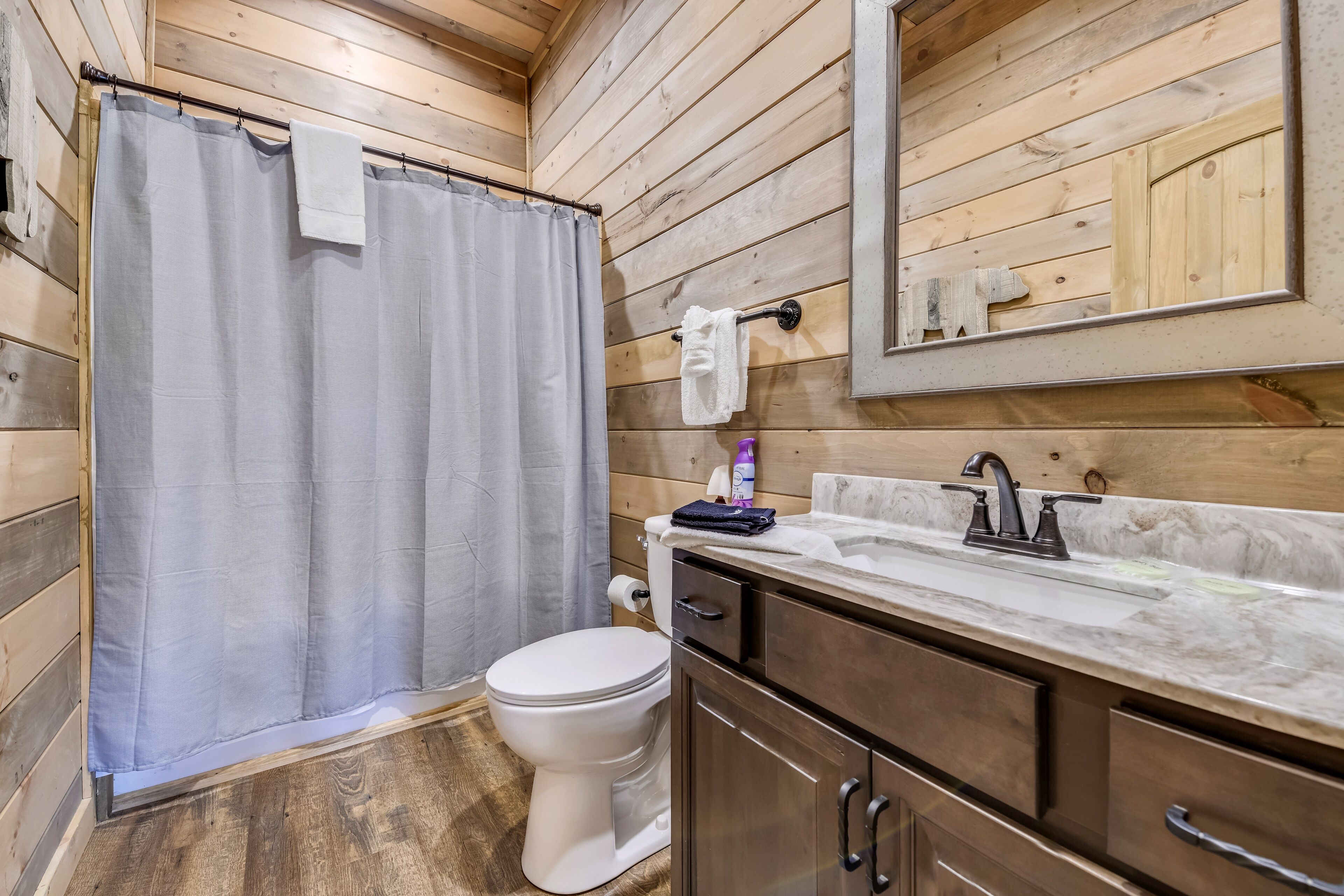 Un baño de cabaña de madera con cortina de ducha, inodoro, lavabo y armarios.