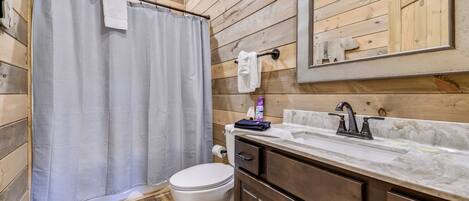 Un baño de cabaña de madera con cortina de ducha, inodoro, lavabo y armarios.