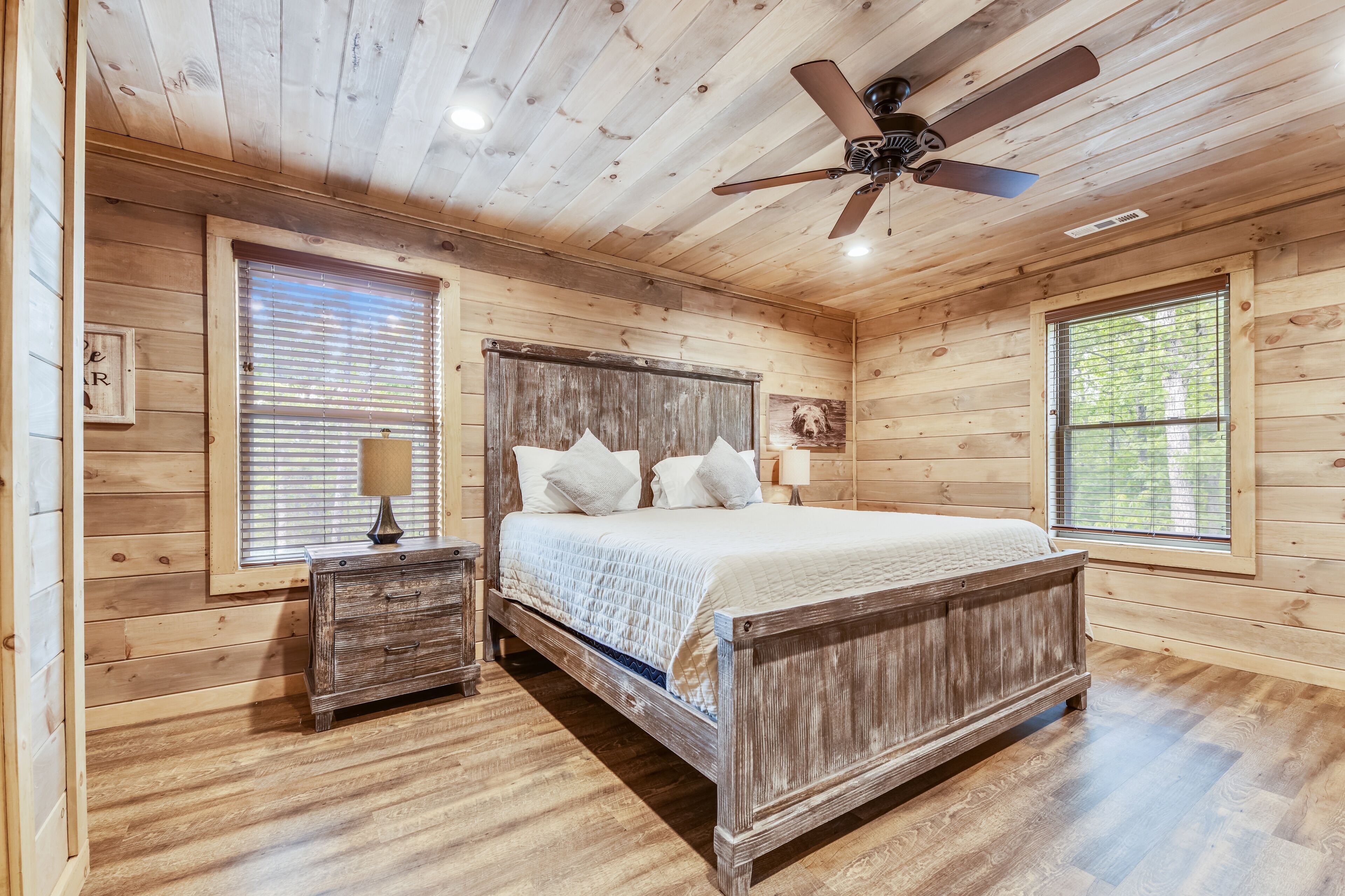 A wooden cabin bedroom with a bed, nightstands, and a ceiling fan.