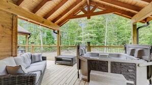 A covered outdoor deck with a hot tub, wicker furniture, and a stone bench.