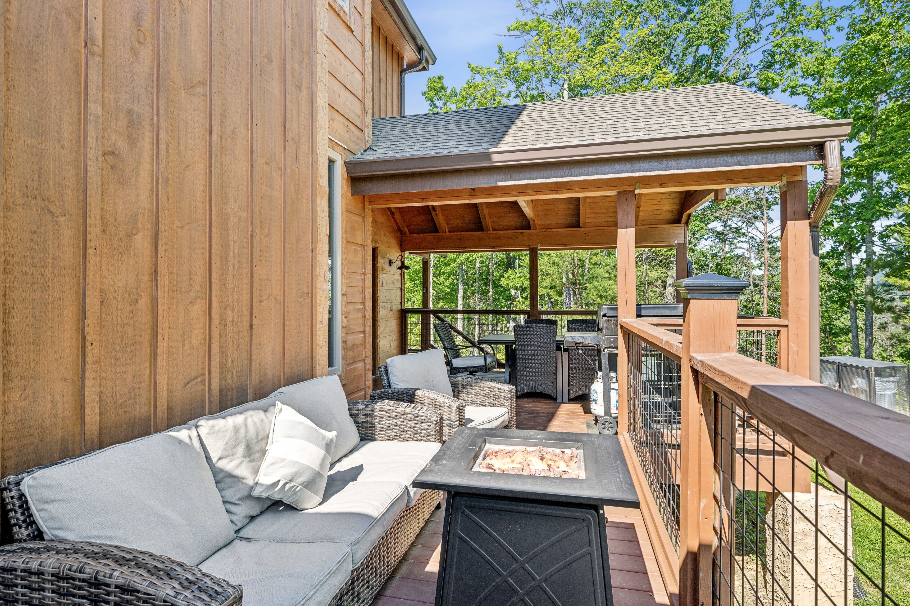 A covered outdoor seating area with wicker furniture, a fire pit, and a view of the surrounding trees.