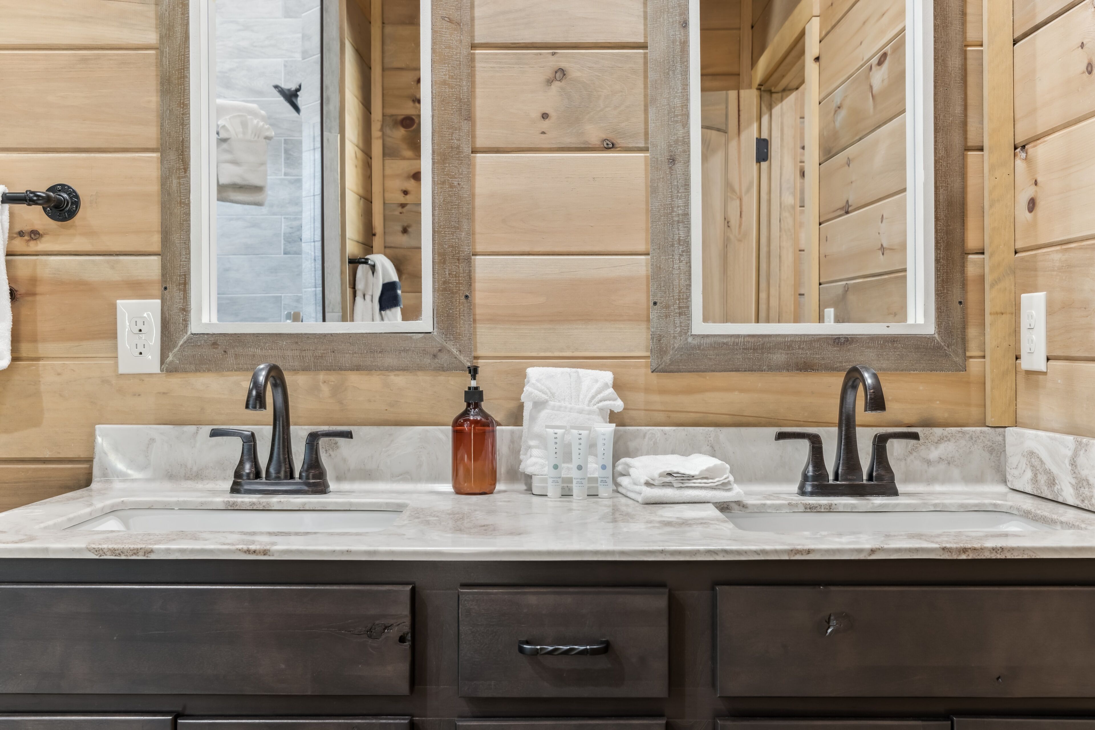 A bathroom with wooden paneling, a double sink with dark faucets, and a mirror above.