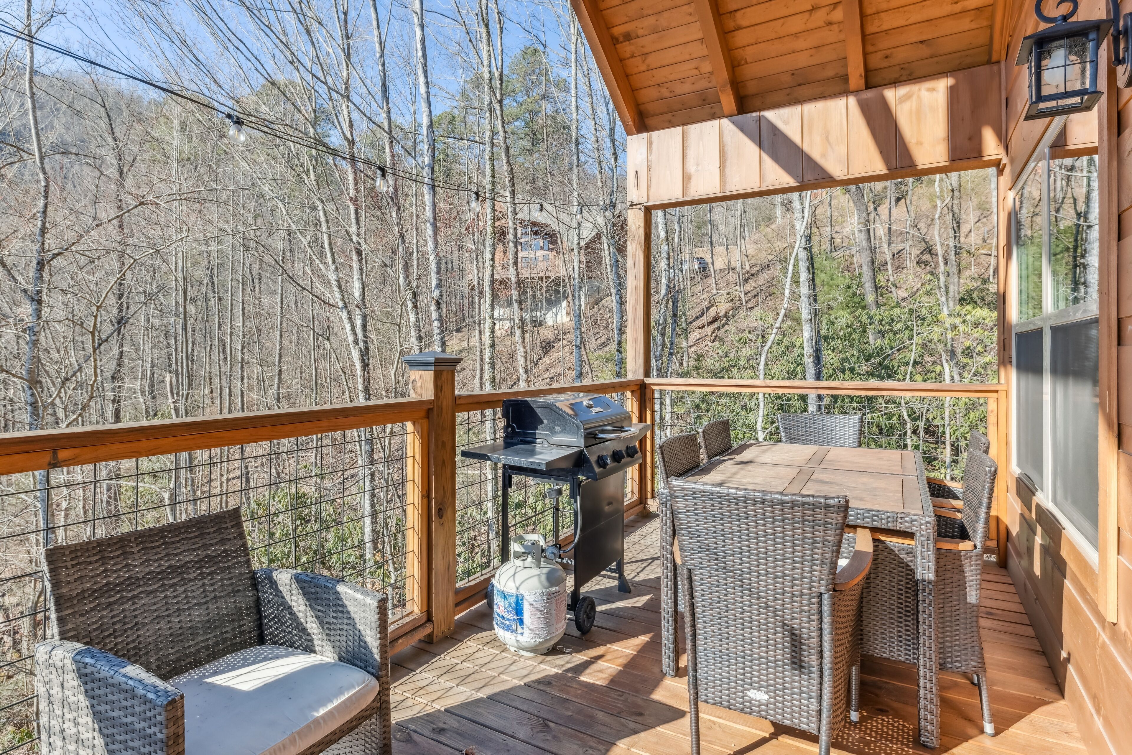 Une terrasse en bois avec des meubles en osier, un barbecue et une bouteille de gaz.