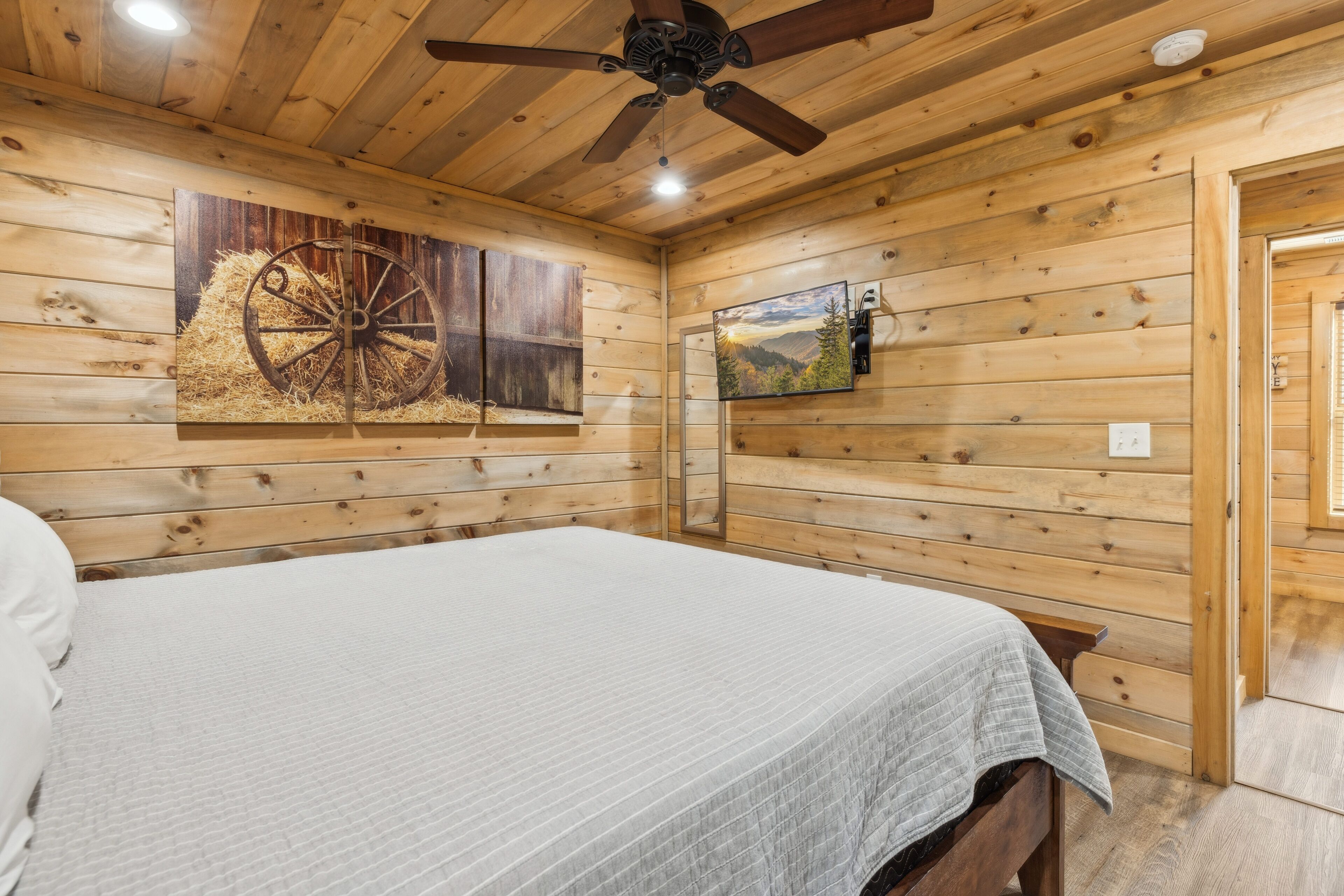 Quarto de cabana de madeira com uma cama, um ventilador de teto e uma televisão fixada na parede.